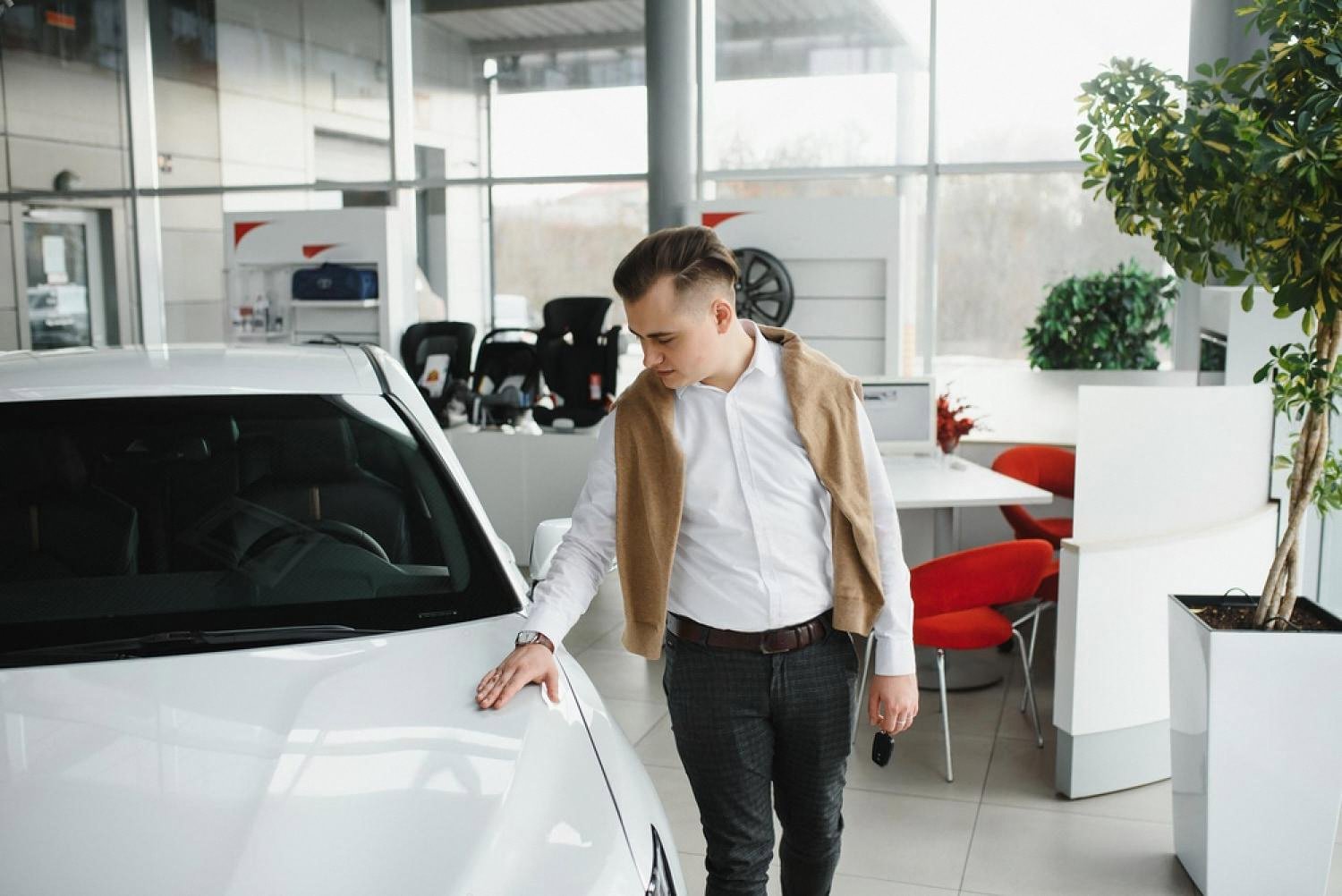 A man in a smart shirt inspecting a white premium car inside a bright rental showroom