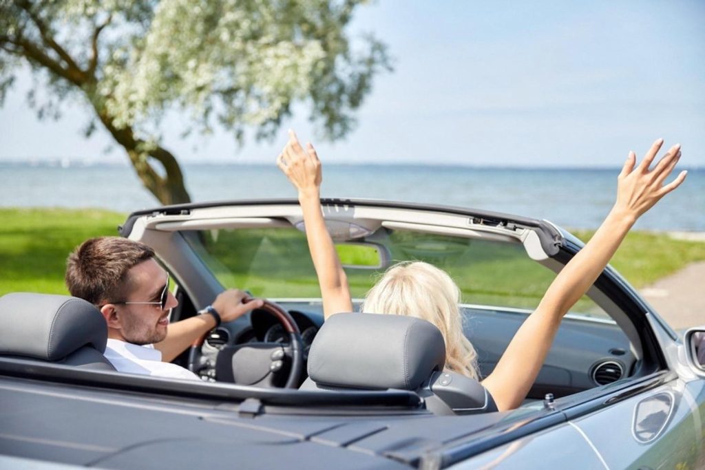A couple enjoying a convertible luxury rental car on a coastal road in Australia with the sea in the background