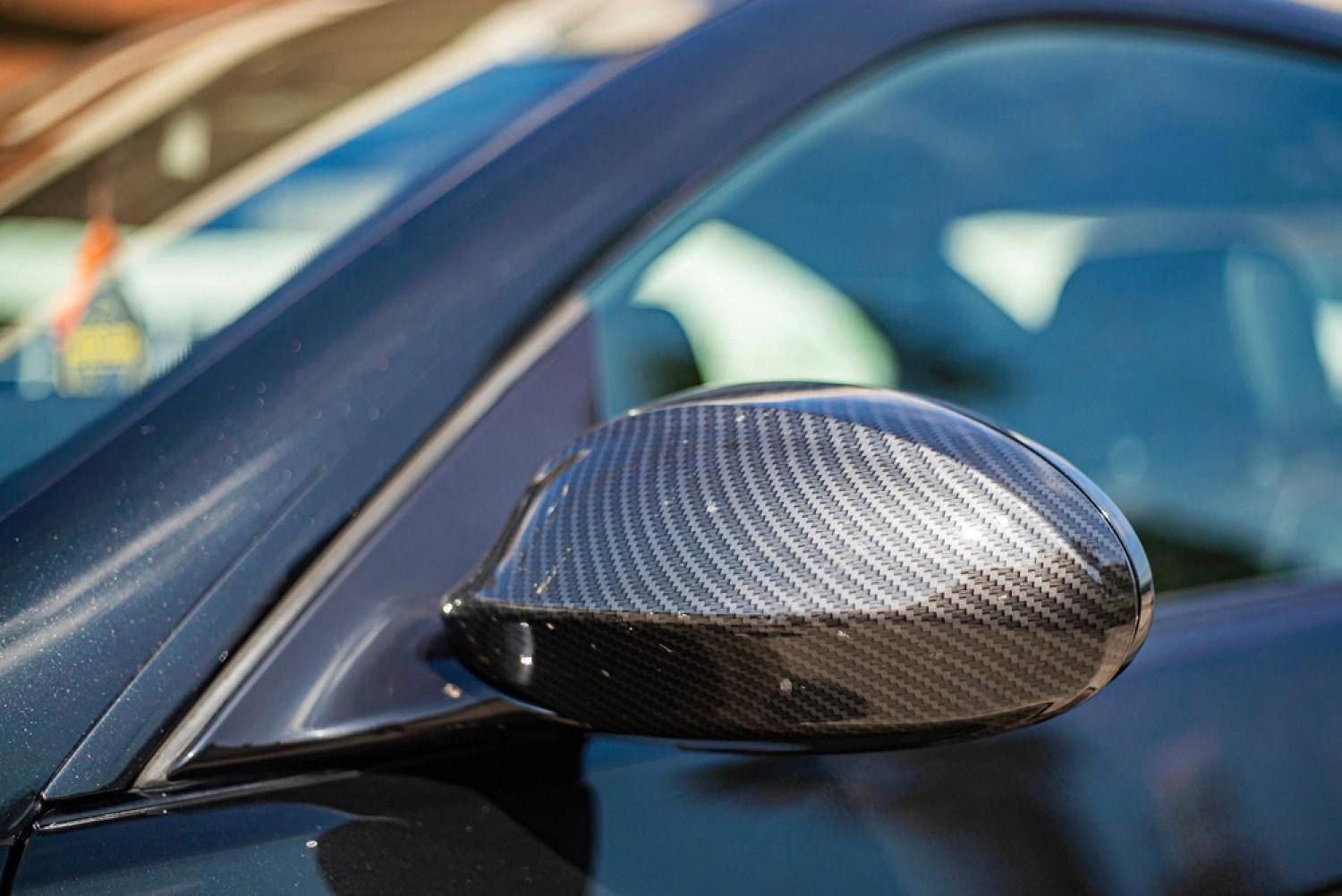 Close-up of a carbon fibre wing mirror on a dark blue luxury car parked on an Australian street